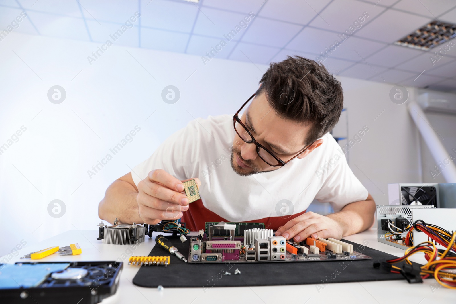 Photo of Male technician repairing motherboard at table indoors