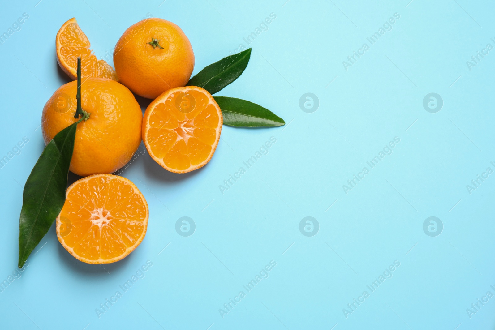 Photo of Flat lay composition with fresh ripe tangerines and leaves on light blue background, space for text. Citrus fruit