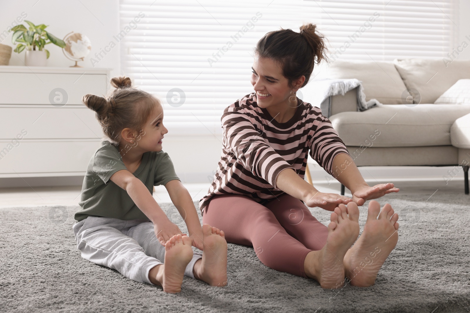 Photo of Young mother and her daughter stretching together at home