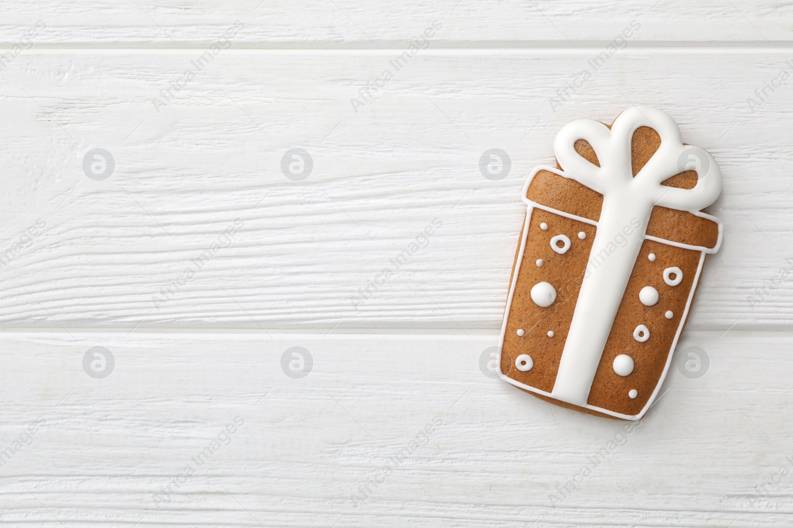 Photo of Gift box shaped Christmas cookie on white wooden table, top view. Space for text