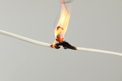 Photo of Inflamed white wire on grey background, closeup. Electrical short circuit