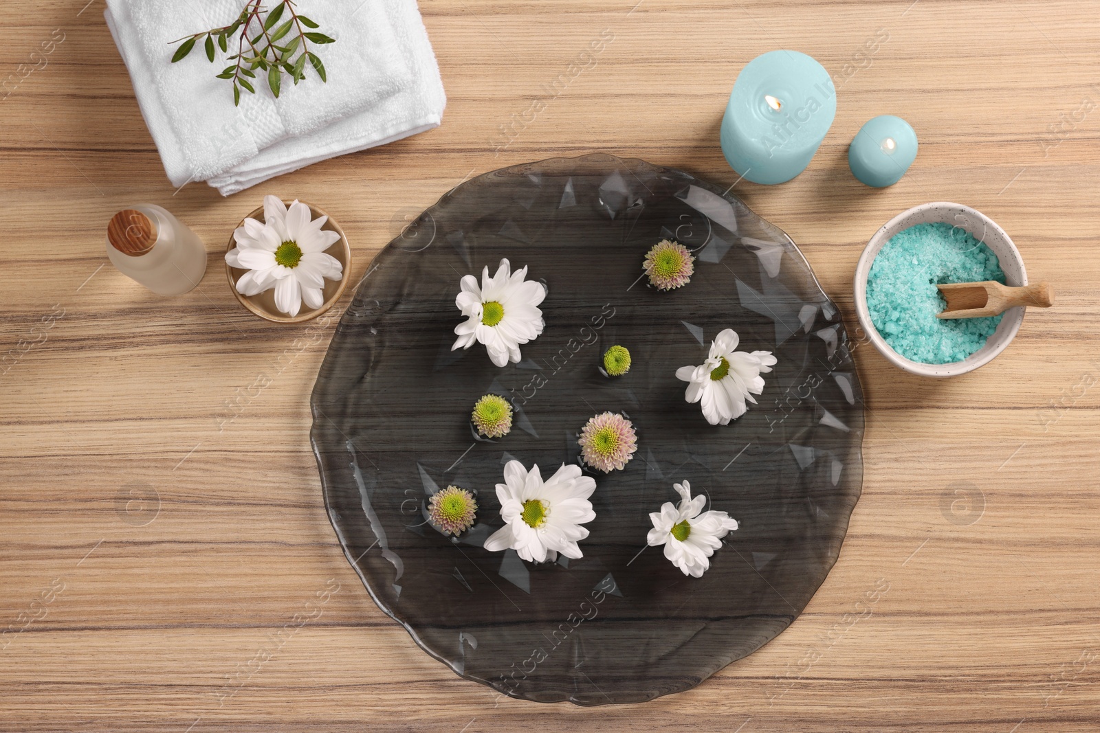 Photo of Plate with water, flowers, burning candles and sea salt on wooden floor, flat lay. Pedicure procedure