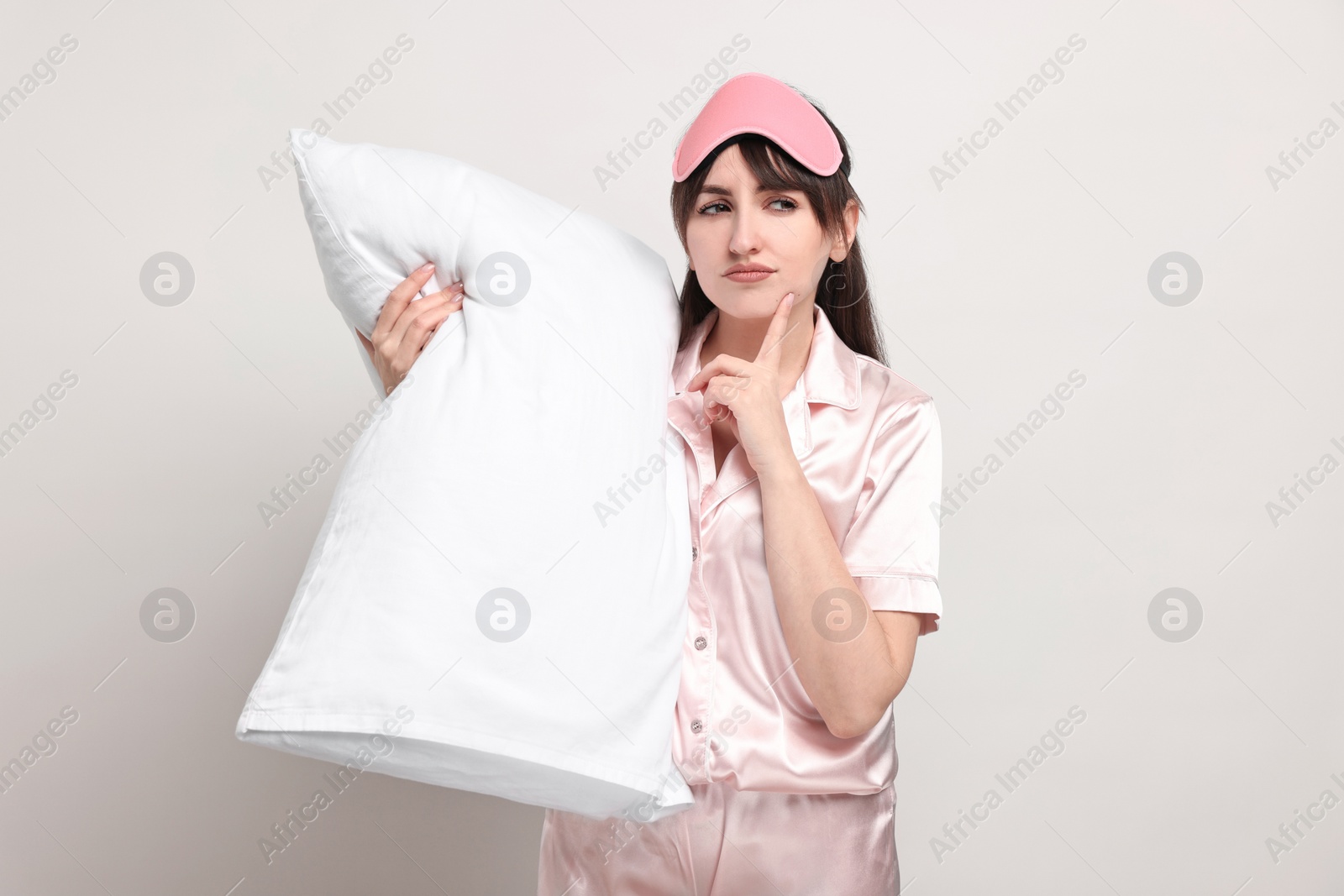 Photo of Woman in pyjama and sleep mask holding pillow on light grey background