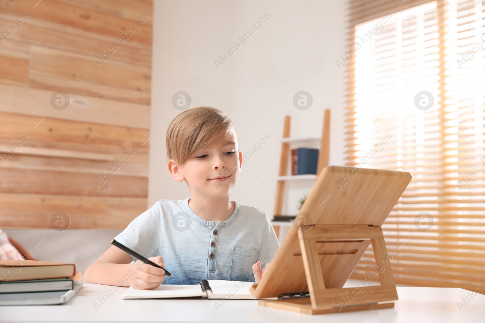 Photo of Boy doing homework with tablet at table indoors