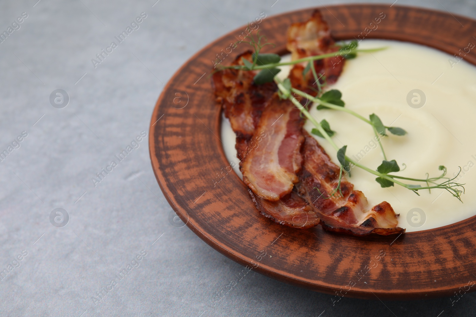 Photo of Delicious potato soup with bacon and microgreens in bowl on gray table, closeup. Space for text