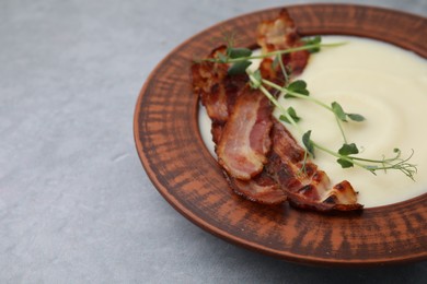 Photo of Delicious potato soup with bacon and microgreens in bowl on gray table, closeup. Space for text