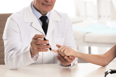 Photo of Doctor taking patient's blood sample with lancet pen in hospital, closeup. Diabetes control