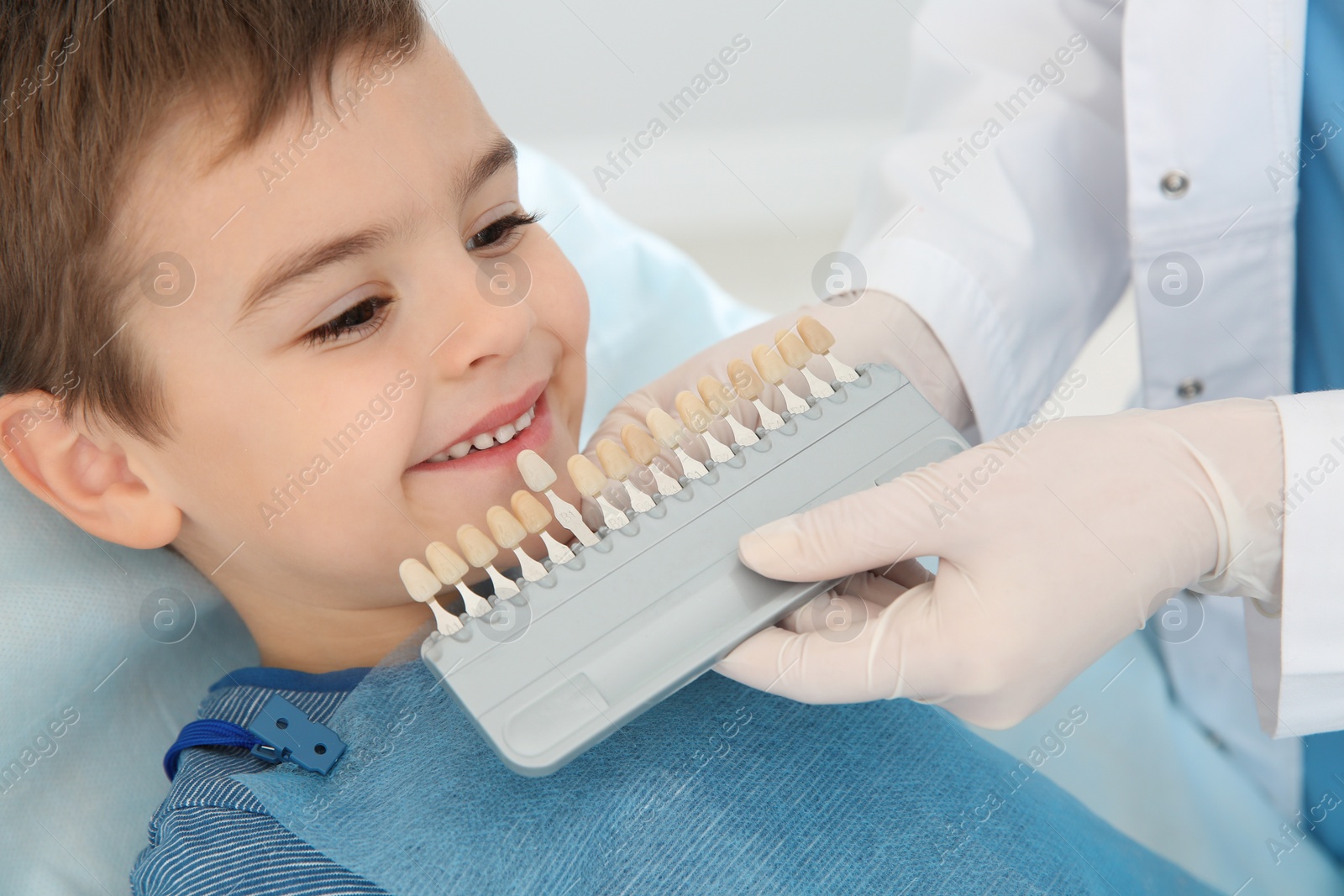 Photo of Dentist selecting cute boy's teeth color with palette in clinic