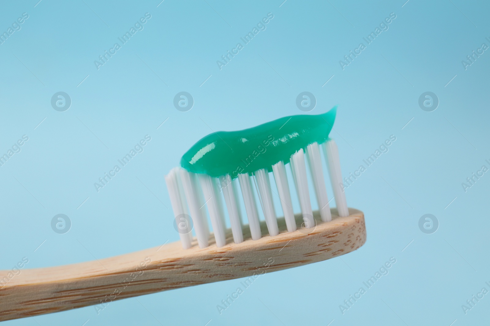 Photo of Wooden brush with toothpaste on light blue background, closeup