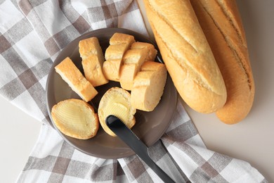 Photo of Whole and cut baguettes with fresh butter on table, flat lay