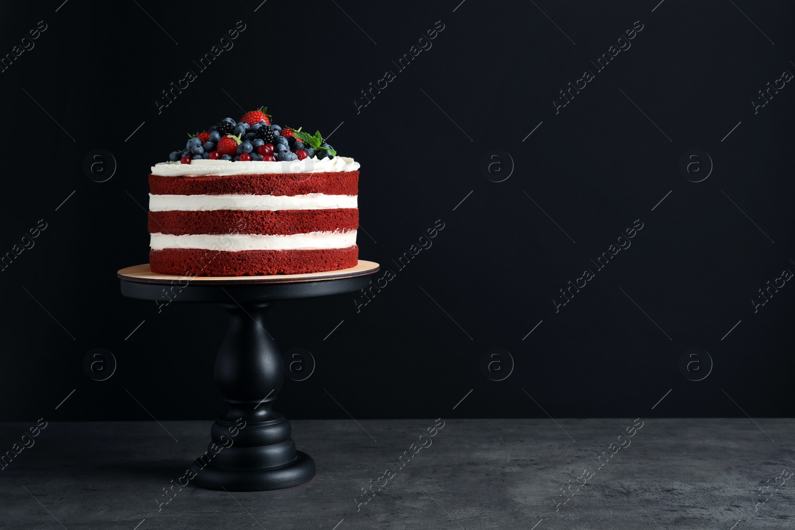 Photo of Stand with delicious homemade red velvet cake and space for text on black background