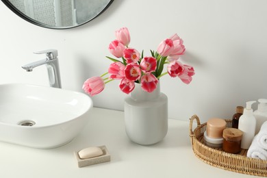 Vase with beautiful pink tulips and toiletries near sink in bathroom