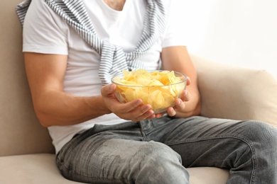 Photo of Man with bowl of potato chips sitting on sofa, closeup