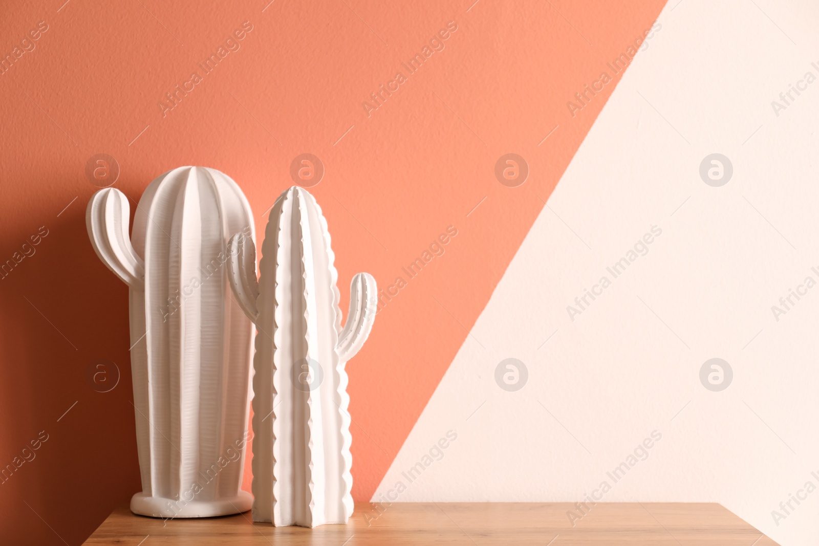 Photo of Decorative ceramic cacti on table near color wall, space for text. Interior decor