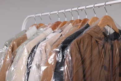 Photo of Dry-cleaning service. Many different clothes in plastic bags hanging on rack against grey background, closeup