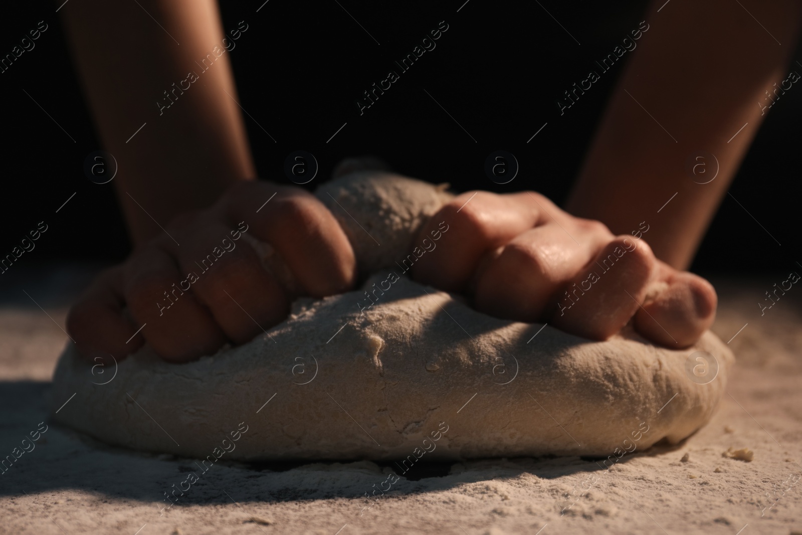 Photo of Making bread. Woman kneading dough at table on dark background, closeup