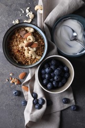 Photo of Tasty granola in bowl, blueberries, yogurt and spoon on gray textured table, flat lay