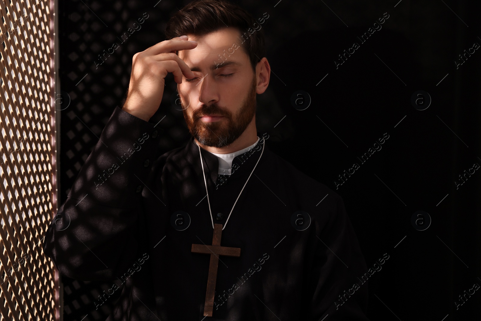 Photo of Catholic priest in cassock crossing himself in confessional