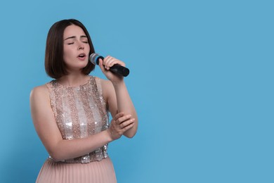 Beautiful young woman with microphone singing on light blue background, space for text