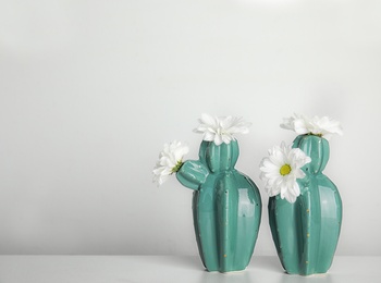 Photo of Trendy cactus shaped vases with flowers on table against light wall. Creative decor