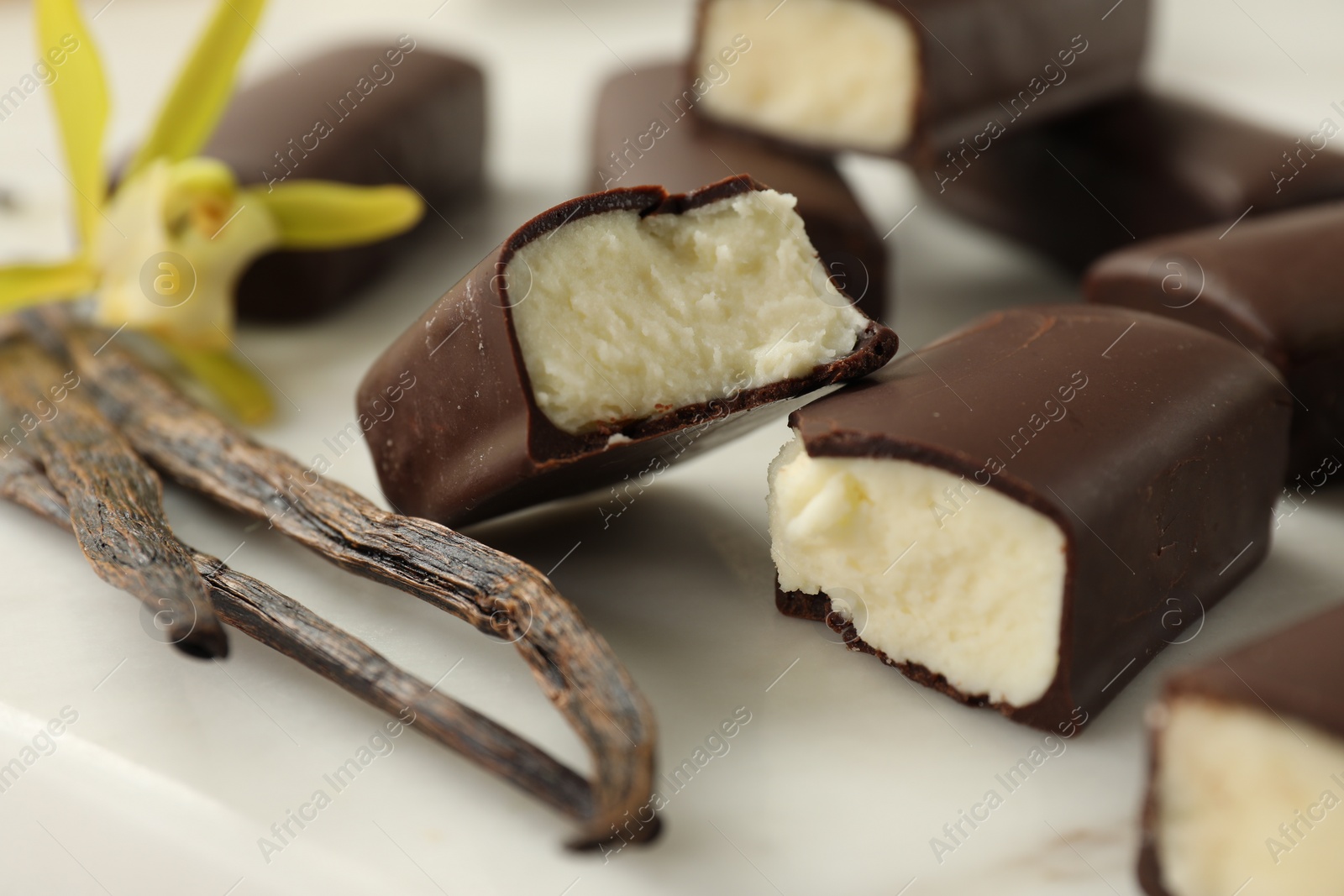 Photo of Glazed curd cheese bars, vanilla pods and flower on white board, closeup