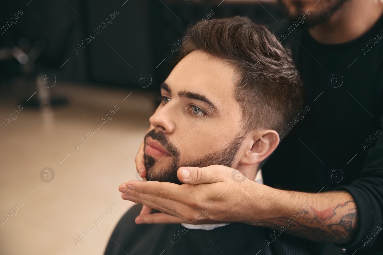 Photo of Hairdresser applying serum onto client's beard in barbershop. Professional shaving service