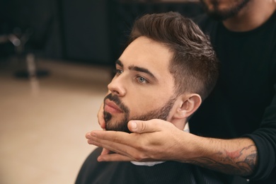 Hairdresser applying serum onto client's beard in barbershop. Professional shaving service