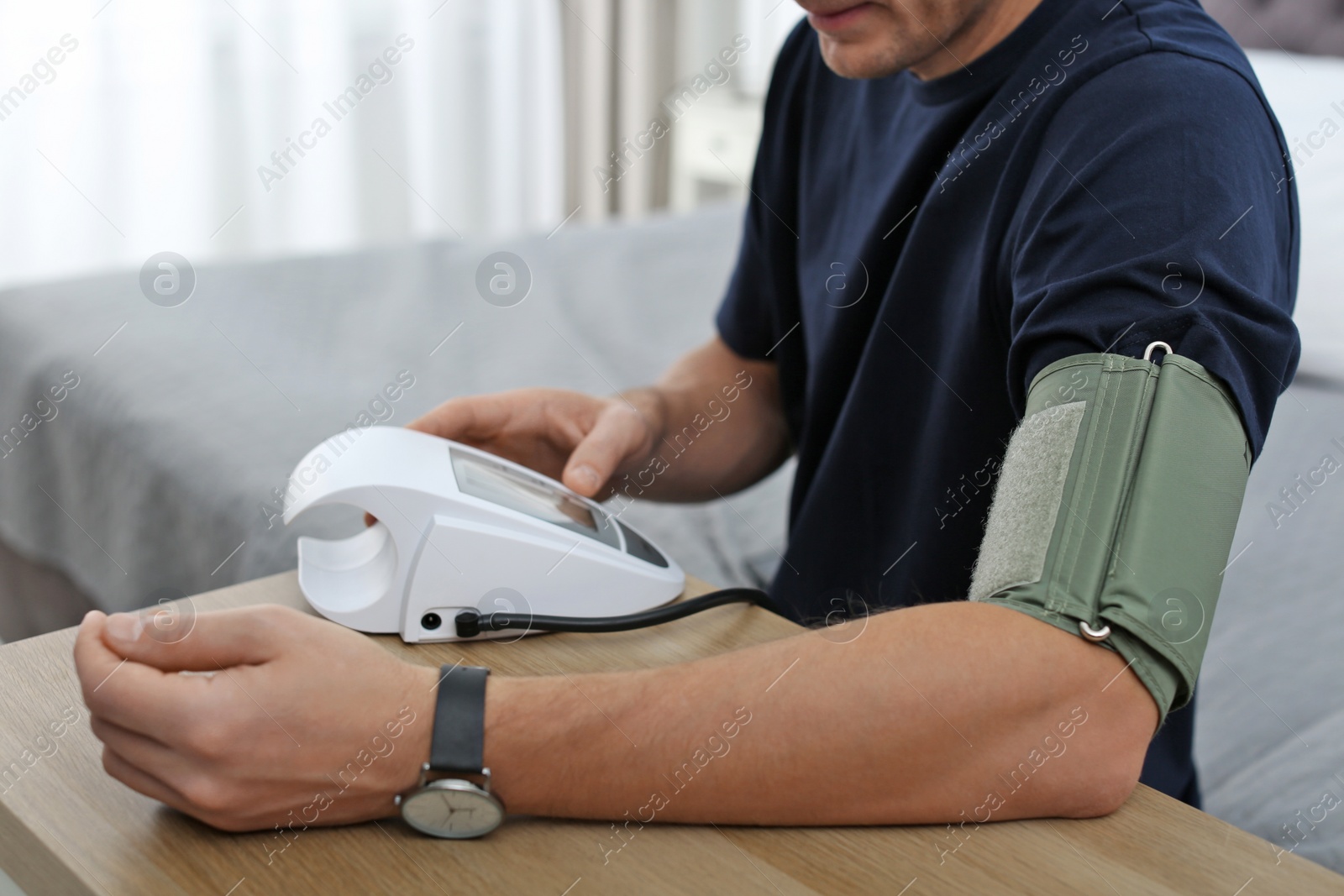 Photo of Man checking blood pressure with sphygmomanometer at table indoors, closeup. Cardiology concept