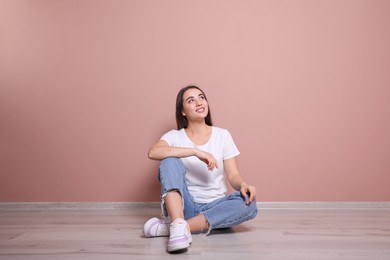 Young woman sitting on floor near pink wall indoors
