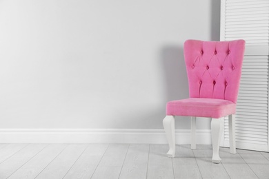 Photo of Stylish pink chair and folding screen near white wall. Space for text