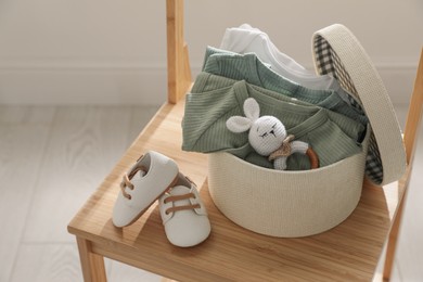 Photo of Box with baby bodysuits, booties and toy on chair indoors