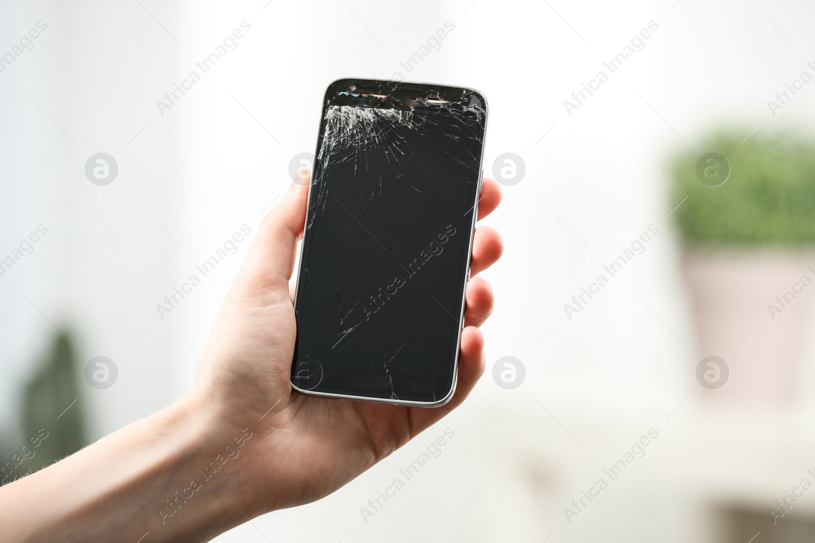 Photo of Woman holding damaged smartphone on blurred background, closeup. Device repairing