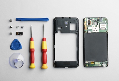 Disassembled mobile phone and repair tools on light background, flat lay