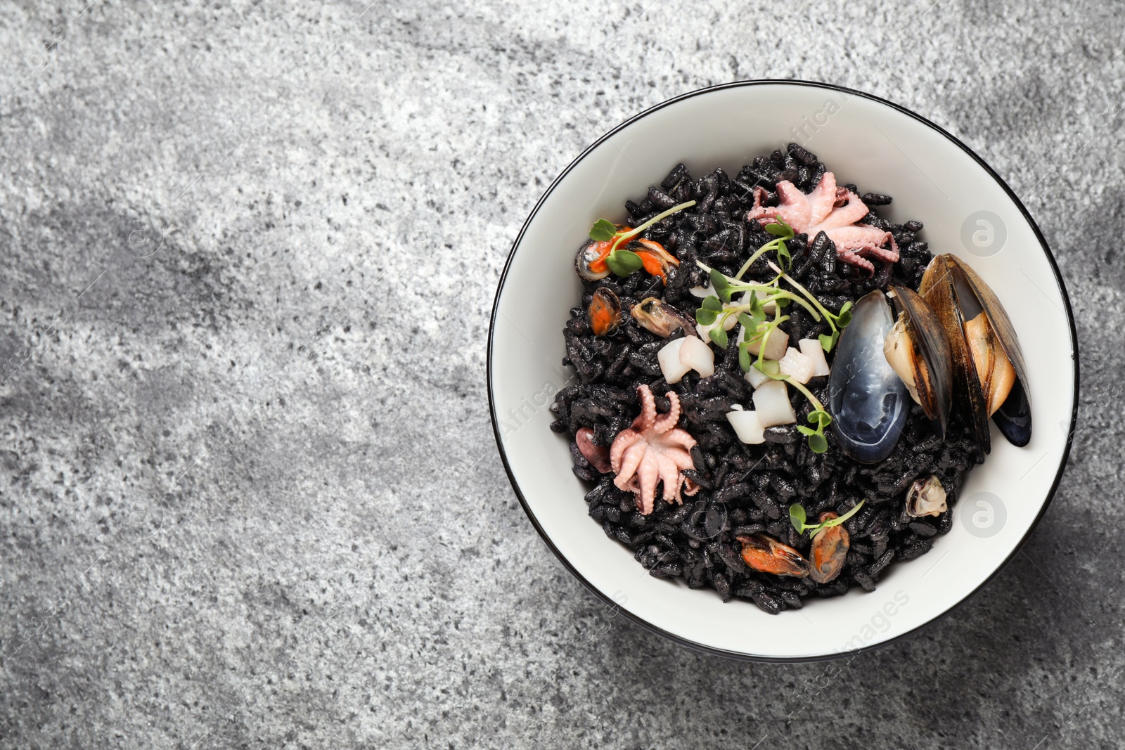 Photo of Delicious black risotto with seafood in bowl on light grey table, top view. Space for text