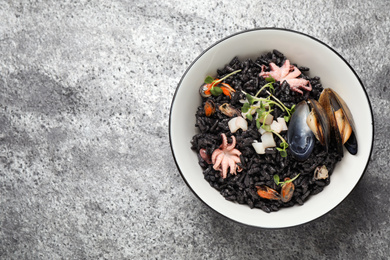 Photo of Delicious black risotto with seafood in bowl on light grey table, top view. Space for text