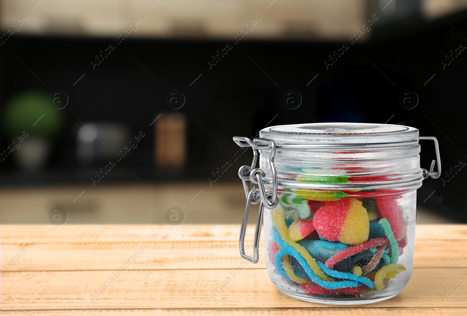 Image of Glass jar with tasty gummy candies on wooden table in kitchen. Space for text