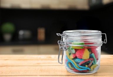 Glass jar with tasty gummy candies on wooden table in kitchen. Space for text