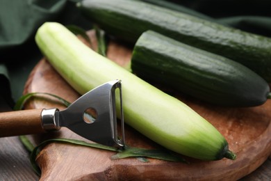 Photo of Fresh cucumbers and peeler on wooden table, closeup