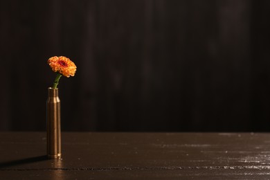 Photo of Beautiful flower in bullet case on wooden table against dark background. Space for text