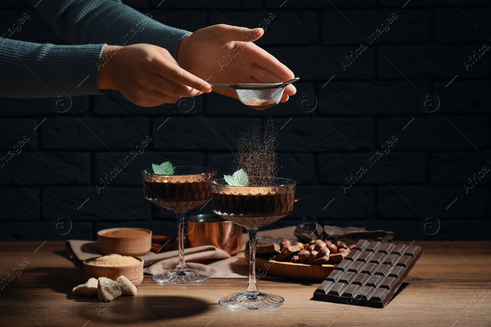 Photo of Woman decorating hot chocolate with cocoa powder at wooden table, closeup