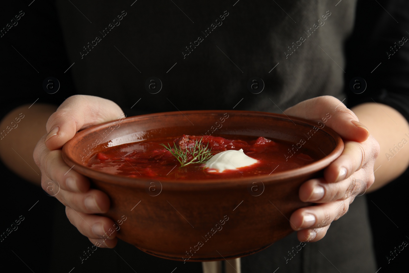 Photo of Woman holding clay bowl with Ukrainian borsch, closeup