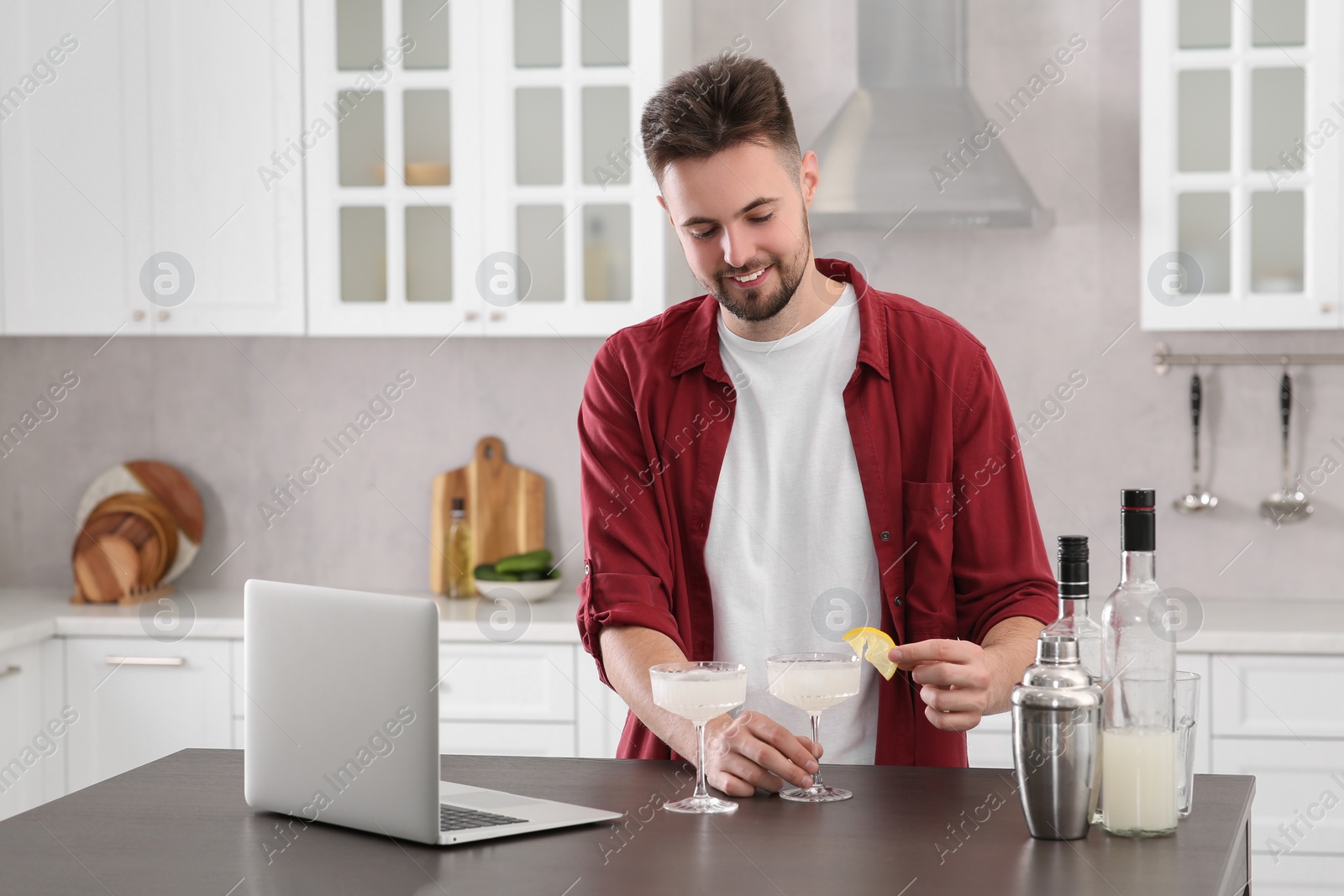 Photo of Man learning to make cocktail with online video on laptop at table in kitchen. Time for hobby