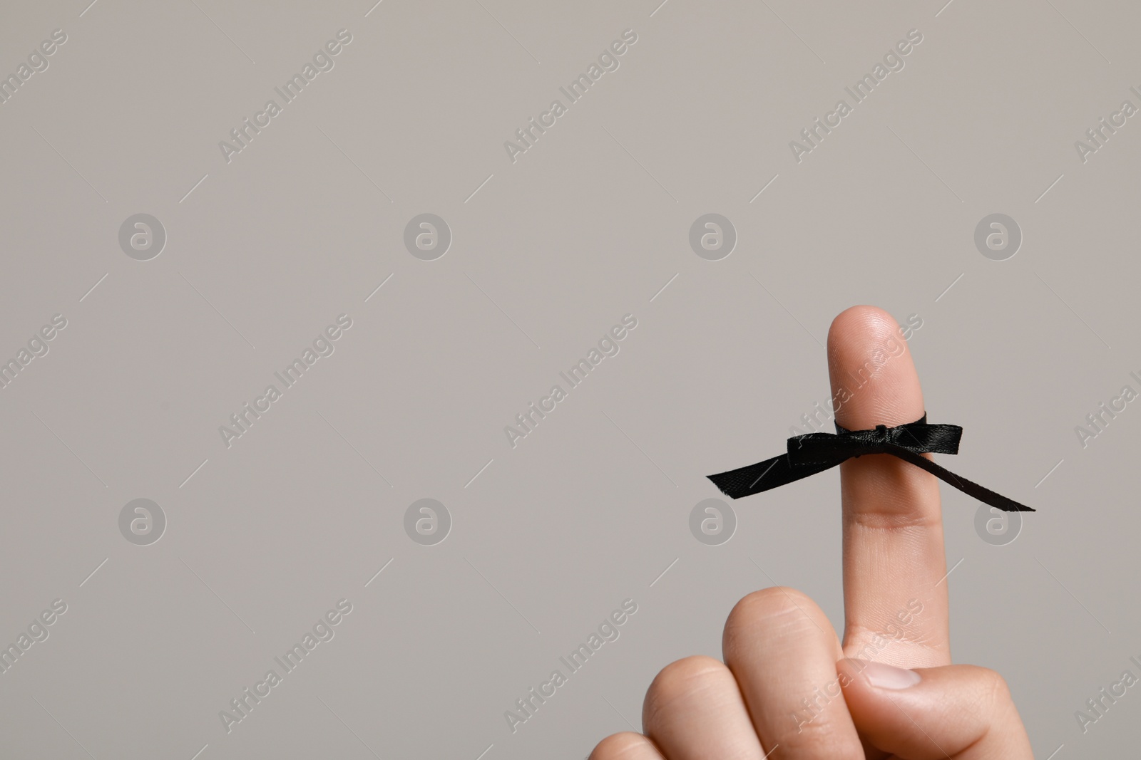Photo of Man showing index finger with black tied bow as reminder on light grey background, closeup. Space for text