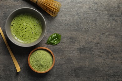 Photo of Cup of fresh matcha tea, bamboo whisk, spoon and green powder on dark grey table, flat lay. Space for text
