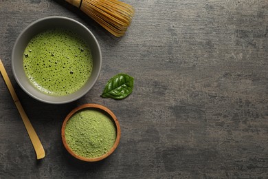 Cup of fresh matcha tea, bamboo whisk, spoon and green powder on dark grey table, flat lay. Space for text