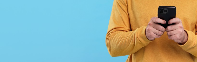 Man typing message on mobile phone against light blue background, closeup. Banner design with space for text