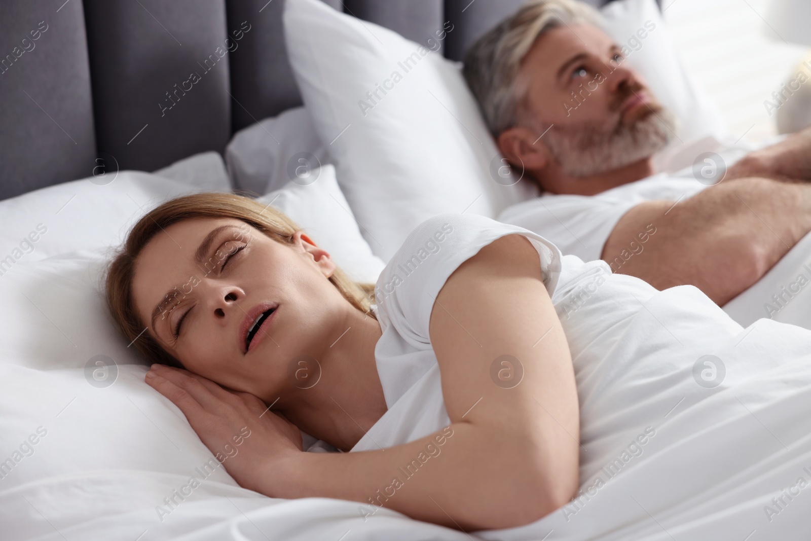 Photo of Irritated man lying near his snoring wife in bed at home