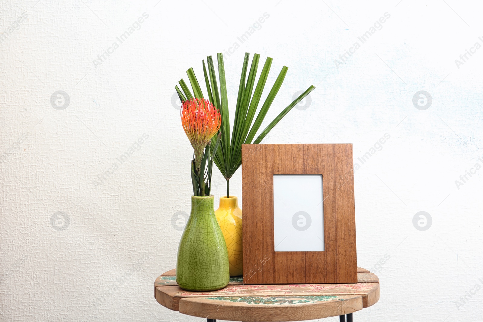 Photo of Blank frame and beautiful plants on table near white wall. Mock up for design