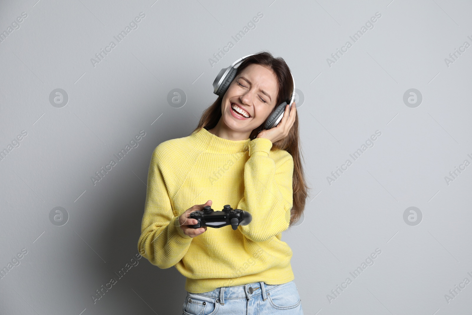 Photo of Happy woman in headphones with game controller on light grey background