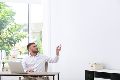 Photo of Young man with air conditioner remote in office